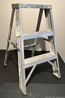 Front angle view of a lightweight aluminum step ladder showing two wide steps, scuffed and scratched surface with paint marks.