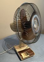 Photo of beige and brown Mastercraft oscillating fan from left side showing blade cage and sliding control buttons on base.