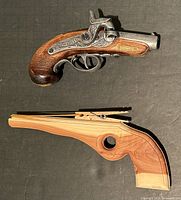 Top view of both items showing the wood-crafted toy pistol with elastic band mechanism and the Philadelphia Derringer replica with engraved metal and wood grip.