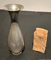 Both vases shown side by side on black surface, pewter vase on left, ceramic paper bag style vase on right