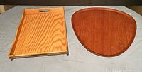 Two wooden Mid-Century Modern trays: a rectangular pine tray and a tear-drop shaped teak tray, both on a grey surface.