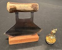 Photo showing the hide scraper with bone handle engraved 'ALASKA' on stand and the small bottle of gold leaf suspended in liquid