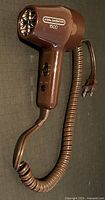 Front angled view of the brown Vidal Sassoon 1500 travel hairdryer showing 2-speed switch and plugged in coiled cord.