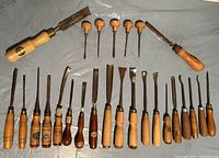Full set of over two dozen vintage wood-carving tools laid out in rows showing the variety of blade shapes and handle styles.