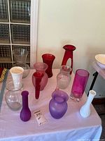 Overview of 13 assorted coloured glass vases on table