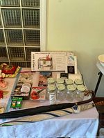 Tabletop view of entire lot including mason jars, boxed wall organizer, packaged lights, blower, adhesives, umbrellas, pillow and drawer pulls