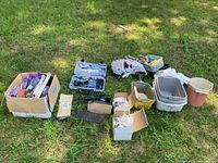 Overview of entire lot spread on grass; shows Dremel case, cardboard boxes with sanding supplies, plastic bins and buckets