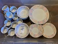Overview of dinnerware in storage bin including bowls, plates and cups