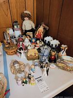 Overall view of table with assorted figurines, doll, lighthouse, vases and plate