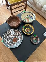 Overview of all five ceramic and pottery plates and bowls on a black surface showing size, shape, and color variations.