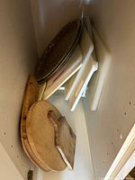Cabinet interior showing multiple white plastic cutting boards, wooden boards and round metal tray