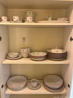 Full view of three shelves showing plates, bowls, lidded dish, serving bowls, platter and cups