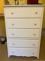 Front view of white five-drawer dresser showing knobs and scalloped base