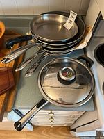 Stack of five stainless frying pans and one lidded pan