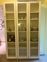 Front view of both tall white IKEA glass-door cabinets with shelves