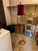 Full view brass-tone floor lamp with burgundy shade, towel rack visible behind