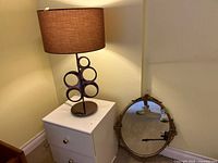 Table lamp on small drawer unit; oval mirror leaning against wall