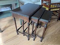 Side stacked view of three dark wood nesting tables with scalloped edges and turned legs.