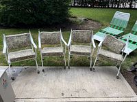 Front view of four white metal patio chairs with patterned cushions on casters
