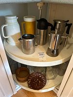 Full view of cabinet shelves showing pitchers, espresso pot, glass canisters and wicker baskets