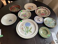 Overview of 10 ceramic plates and bowls with various floral and nature-themed designs on a dark wooden table.