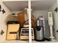 Cabinet view showing popcorn maker, blender base and jar, coffee grinder, Braun immersion blender, wooden board