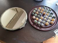 Wood solitaire board with stone marbles and mirrored pedestal side by side