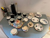 All teacups, saucers, coffee set and lustreware pieces arranged on counter