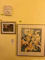 Photo showing all three items mounted on yellow wall: plaster portrait plaque, framed fabric art, and framed watercolour painting of irises