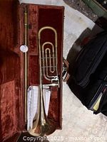 Open case showing trombone slide, bell section and mouthpiece container with sheet music