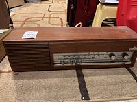 Front view showing speaker grill, tuning dial with AM/FM scale, control knobs, and push buttons showing overall condition and wear for the wooden radio.