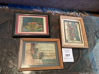 Three framed artworks displayed on a carved wooden surface, showing overall lot contents
