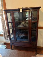 Front view of antique oak glass cabinet showing glass doors, three shelves inside, and short tapered legs.