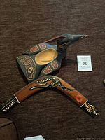 Top view of the hand-carved bird-shaped wooden bowl next to the hand-painted boomerang on a brown fabric surface.
