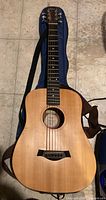 Full front view of Baby Taylor guitar on tile floor with case beneath