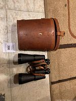 Full view of binoculars laid out next to the closed leather case on tiled floor.