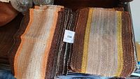 Set of handwoven placemats showing both yellow and orange striped designs, earthy tones with woven texture.