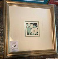 Framed lithograph featuring floral artwork with white camellia flowers and green leaves, mounted in a gold-tone frame with off-white matting.