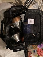 Birds-eye view of black carrying bag unzipped, showing copper and silver Denis Wick trombone mutes inside.