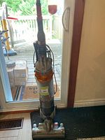 Front view of the Dyson upright vacuum cleaner showing the clear dust bin, orange filter, and red handle.