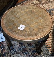 Angled view of round table showing embossed brass top and claw feet
