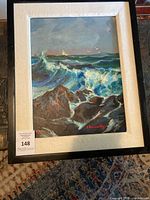 Framed painting showing ocean waves and rocks with sailboat, signed E. Baraoski.