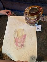 Murano handblown glass sculpture with amber, pink, purple and clear coloring, shown next to the original hand drawing and authenticity certificate on a table.