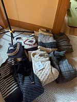 Nine folded men's sweaters on carpet near wall and door corner, showing assorted patterns and textures.
