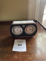 Front view of black plastic thermometer and humidity gauge showing two circular dials for temperature and humidity.