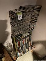 Two tall stacks and a lower shelf of CDs in jewel cases against a wall. Includes label sticker on stack.