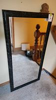 Full view of large rectangular mirror with black marble-effect frame leaning against a wall showing size and overall condition.