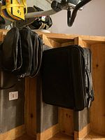 Black medium-sized suitcase and black shoulder bag placed on wooden steps, showing minor wear and material details.