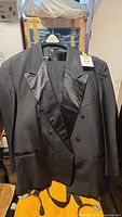 Front view of black tuxedo jacket hanging on a hanger. Visible double-breasted buttons and satin-lapel detail.