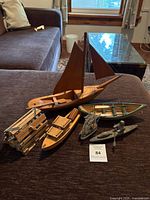 Six wooden model boats displayed on a brown fabric surface indoors, showing a variety of shapes and sizes.